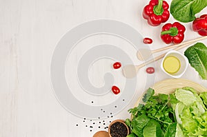 Fresh green vegetables, greens, red cherry tomatoes and kitchenware on soft white wood board, border, top view.