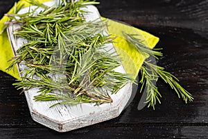 Fresh greens. Green sprigs of rosemary. Seasoning for meat and other products. On a light wooden board. On a dark background