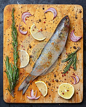 Fresh grey mullet fish lies on light wooden cutting board with l