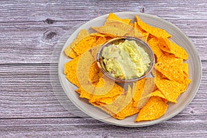 Fresh guacamole in a bowl with corn tortilla chips on a plate on a wooden table. Mexican cuisine ingredients. Top view with copy