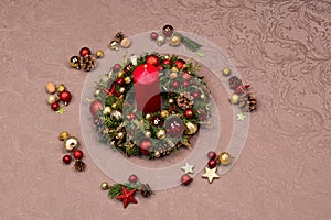Fresh handmade Christmas wreath decorated with red and gold Christmas decorations, fir-cones and walnuts with a red burning candle