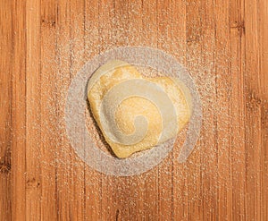 Fresh,handmade,single raviolo in the shape of heart,covered with flour and placed on the wooden table and covered with flour.