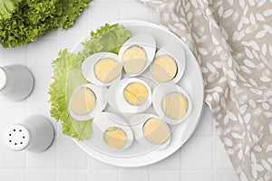 Fresh hard boiled eggs and lettuce on white tiled table, flat lay