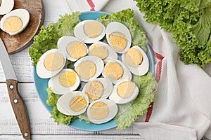 Fresh hard boiled eggs and lettuce on white wooden table, flat lay