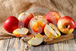 Fresh harvesting red apples on wooden board over canvas bag