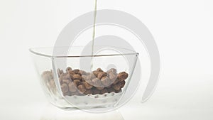 Fresh healthy food. Milk pouring into transparent bowl with chocolate cereal balls on a white background