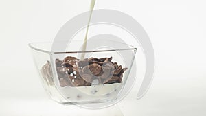 Fresh healthy food. Milk pouring into transparent bowl with chocolate cereal flakes on a white background. The concept of health