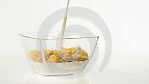 Fresh healthy food. Milk pouring into transparent bowl with yellow cereal cornflakes on a white background