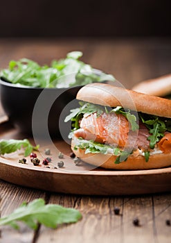 Fresh healthy organic sandwich with salmon and bagel, cream cheese and wild rocket in plate on wooden table background