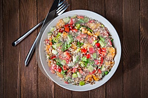 Fresh healthy salad with quinoa, colorful tomatoes, sweet pepper, cucumber and parsley on wooden background top view.