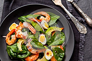 Fresh, healthy salad with shrimps, spinach and avocado on a black background. Top view.