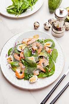 Fresh, healthy salad with shrimps, spinach and avocado on a marble table