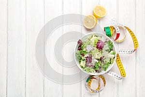 Fresh healthy salad, utensils and tape measure over white wooden