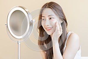 Fresh healthy skin, beautiful smile of asian young woman, girl looking at mirror, applying moisturizer on her face, putting cream