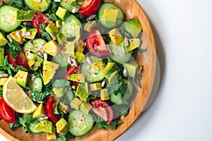 Fresh and healthy summer salad with cucumbers, tomatoes, avocado, arugula, sunflower seeds, lemons and chili flakes.