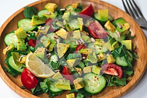 Fresh and healthy summer salad with cucumbers, tomatoes, avocado, arugula, sunflower seeds, lemons and chili flakes.