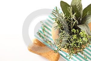 Fresh herbs bouquet in wooden mortar on folded kitchen towel, on white background.