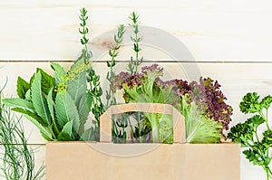 Fresh herbs, onions, parsley, dill, lettuce, mint, rosemary in eco paper bag on wooden background. food delivery.