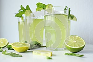 Fresh home-made lemonade with lemon, lime and mint in a glass on white background and ingredients laying on the table