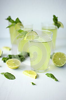 Fresh home-made lemonade with lemon, lime and mint in a glass on white background and ingredients laying on the table