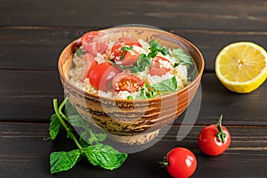 Fresh home-made tabouli, or tabbouleh salad, with its ingredients, side view on dark wooden background