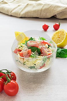 Fresh home-made tabouli, or tabbouleh salad, with its ingredients, side view on grey background