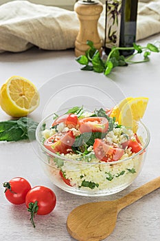 Fresh home-made tabouli, or tabbouleh salad, with its ingredients, side view on grey background