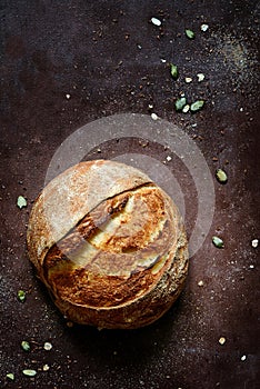 Fresh homemade bread from whole wheat and rye flour with flax seeds, pumpkin and oat flakes on a brown background.