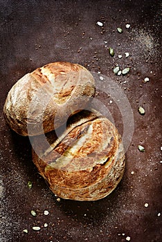 Fresh homemade bread from whole wheat and rye flour with flax seeds, pumpkin and oat flakes on a brown background.