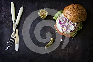 Fresh homemade burger with spicy sauce,cornichons and herbs over dark metal background