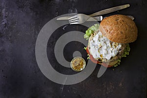 Fresh homemade burger with spicy sauce,cornichons and herbs over dark metal background