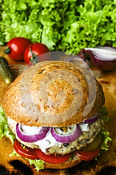 Fresh homemade burger with spicy sauce,cornichons and herbs over dark metal background