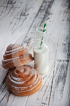 Fresh homemade cinnamon rolls on a wooden cutting desk and milk in glass bottle