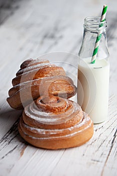 Fresh homemade cinnamon rolls on a wooden cutting desk and milk in glass bottle