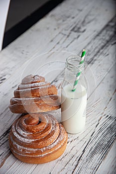 Fresh homemade cinnamon rolls on a wooden cutting desk and milk in glass bottle