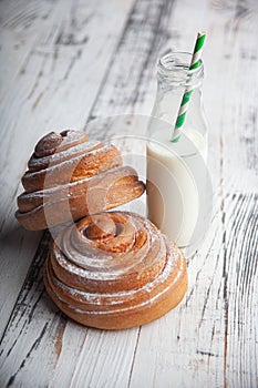 Fresh homemade cinnamon rolls on a wooden cutting desk and milk in glass bottle