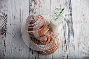 Fresh homemade cinnamon rolls on a wooden cutting desk and milk in glass bottle