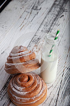 Fresh homemade cinnamon rolls on a wooden white desk and milk in glass bottle