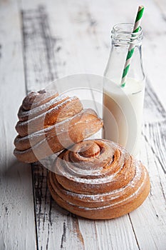 Fresh homemade cinnamon rolls on a wooden white desk and milk in glass bottle