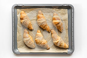 Fresh homemade croissants on baking tray with baking paper. French bakery concept