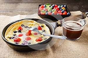 Fresh homemade dutch baby pancake with blueberry raspberry and strawberry in a pan on a table.