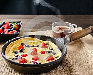 Fresh homemade dutch baby pancake with blueberry raspberry and strawberry in a pan on a table.