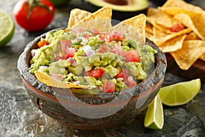 Fresh Homemade Guacamole in Traditional Molcajete with Tortilla Chips, Lime, and Tomato on Rustic Stone Surface