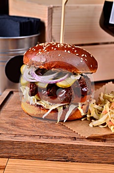Fresh homemade hamburger with beef, onion, sause and cabbage garnish on a wooden board, wooden table background. Juicey