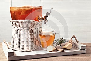 Fresh homemade kombucha fermented tea drink in a jar with faucet and in a cup on a white tray on a wooden background