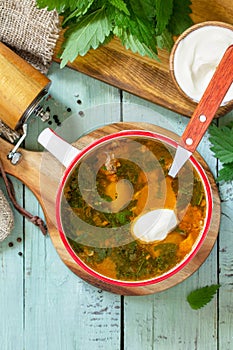 Fresh homemade nettle and meat soup served with sour cream on a rustic table. Top view flat lay.