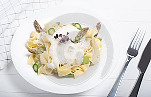 Fresh homemade pasta dish of fettuccine or tagliatelle, green asparagus, white sauce, white plate