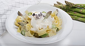 Fresh homemade pasta dish of fettuccine or tagliatelle, green asparagus, white sauce, white plate