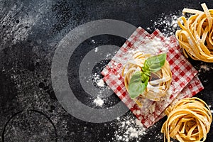 Fresh homemade pasta tagliatelle on wooden spoon with pasta ingredients tomatoes, raw egg, basil leaf on the dark concrete backgro