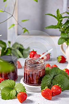 Fresh homemade strawberry jam in glass jar on a light background